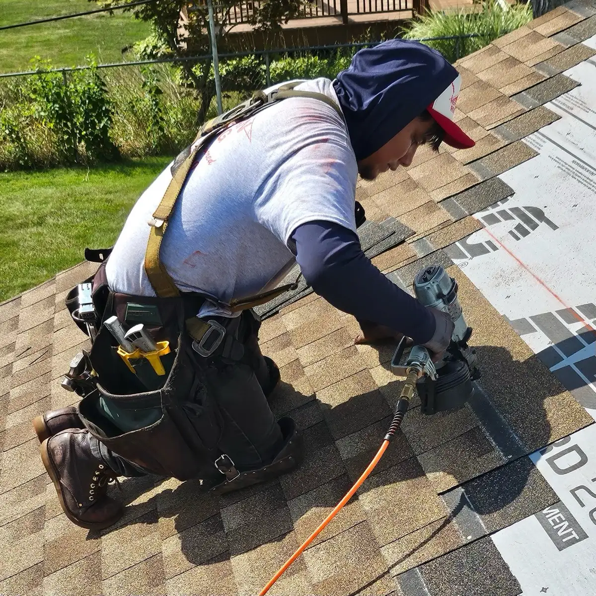 Hefferan roofer installing shingles on a residential roof, kneeling with a nail gun